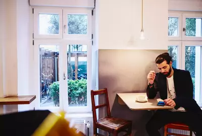 male sitting at table with a coffee, looking seriously at his phone.
